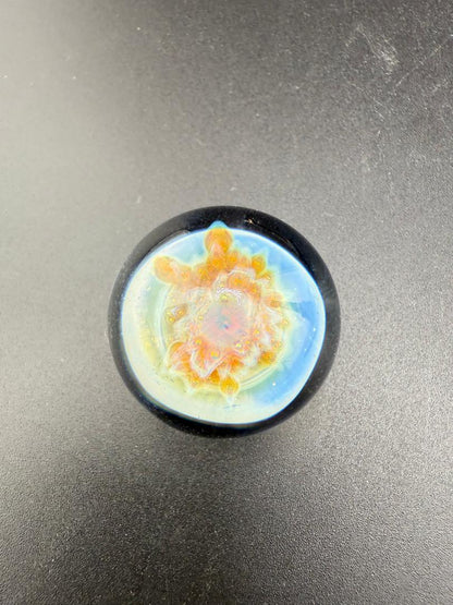 Mcdoogle Glass Marble - 22mm No Fume Fume Tech w/ Purple Flower Dot Stack Backer on a dark surface.