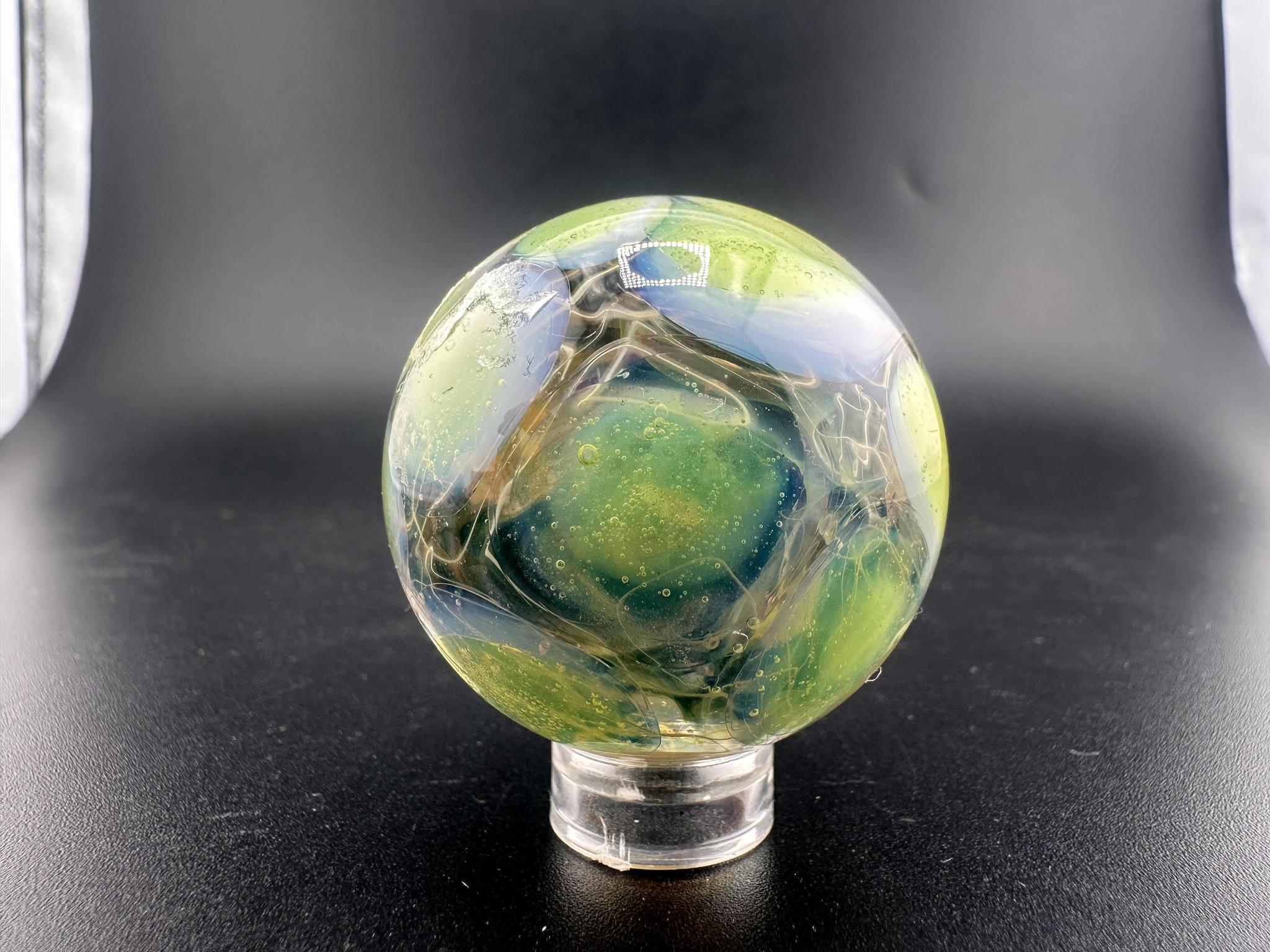 Mop Head Glass Marble - Fumed Implosion Swirl showcased on a stand, featuring vibrant colors and swirling designs.