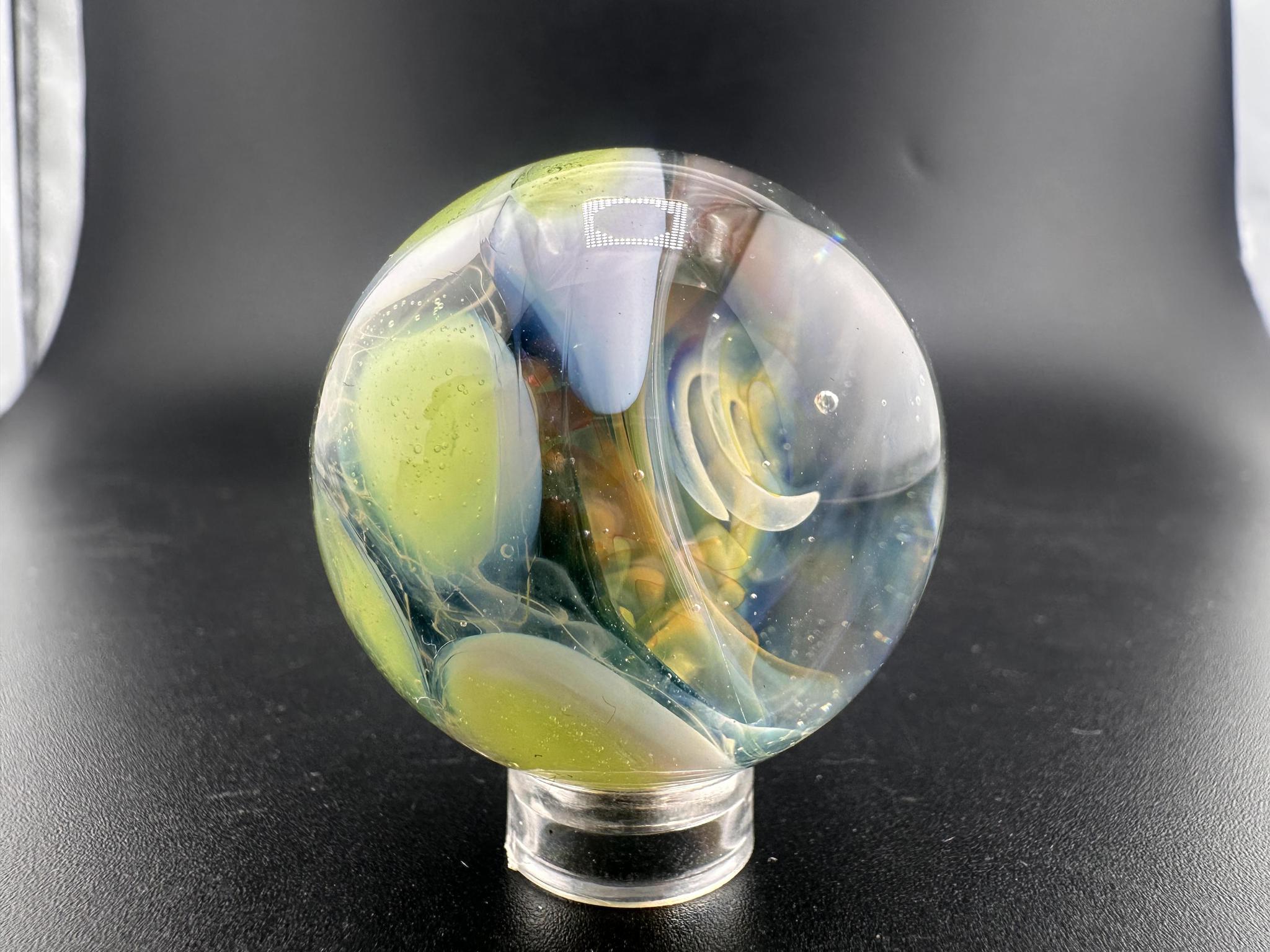 Mop Head Glass Marble - Fumed Implosion Swirl with vibrant colors and swirling design on a display stand.