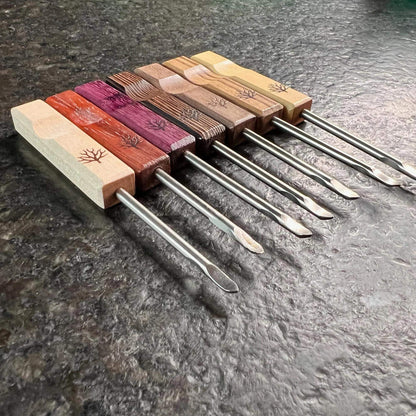 Mystic Timber Dab Tool - Pocket Pick displayed with various wooden handles and metal tips on a dark countertop.