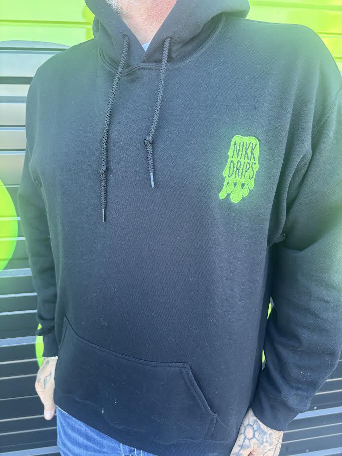 Nikk Drips Hoodie featuring a black design and vibrant green logo on a person, showcasing street-ready style.
