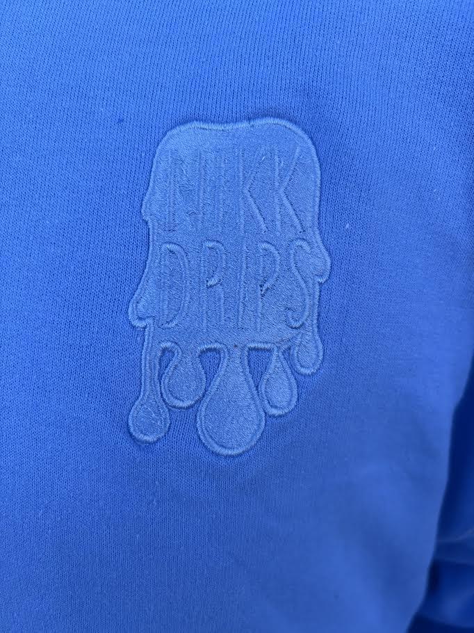 Nikk Drips Hoodie logo on blue fabric, showcasing stylish design and branding.