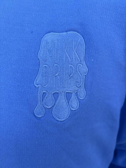 Nikk Drips Hoodie logo on blue fabric, showcasing stylish design and branding.