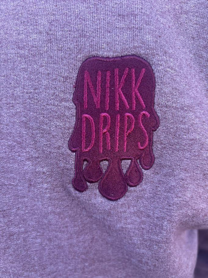 Nikk Drips Hoodie logo detail featuring embroidered text in pink on gray fabric.