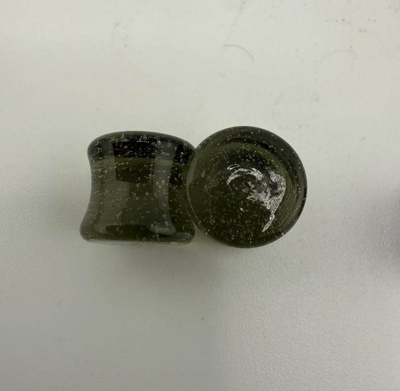 Handcrafted 10mm borosilicate glass ear plugs in dark green color, showcasing unique speckled texture, made in Spokane, WA.