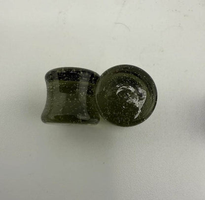 Handcrafted 10mm borosilicate glass ear plugs in dark green color, showcasing unique speckled texture, made in Spokane, WA.