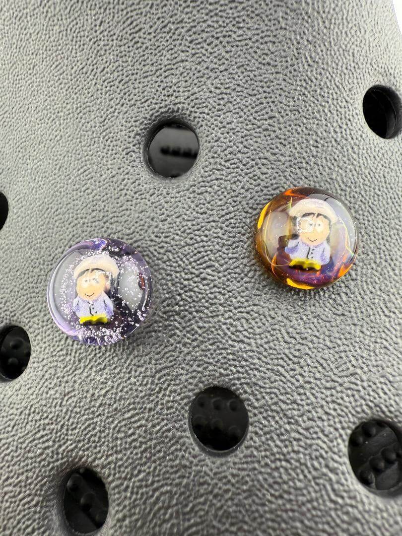 Two handcrafted Paulson Pieces Glass Millie Kroc Giblets featuring pop culture designs on a textured background.