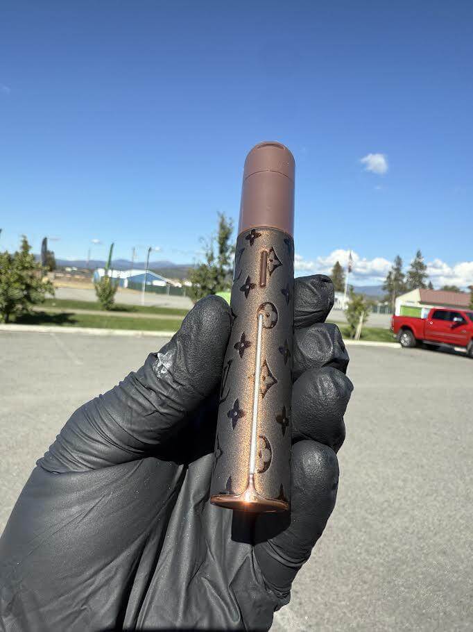 Puffco X Palmers Powders Pivot - LV Power Coated held in a gloved hand outdoors with a scenic background.