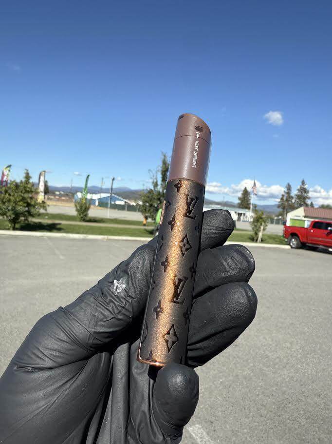 Puffco X Palmers Powders Pivot - LV Power Coated device held in hand against clear sky background.