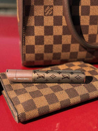 Puffco X Palmers Powders Pivot - LV Power Coated resting on a checkered Louis Vuitton wallet and bag.