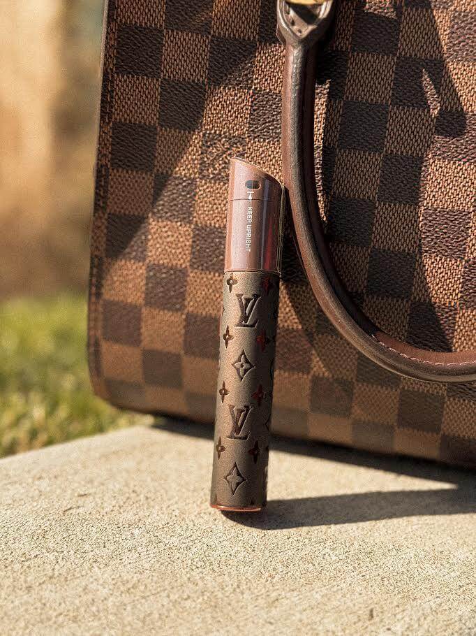Puffco X Palmers Powders Pivot - LV Power Coated next to a stylish Louis Vuitton handbag on a sunny day.