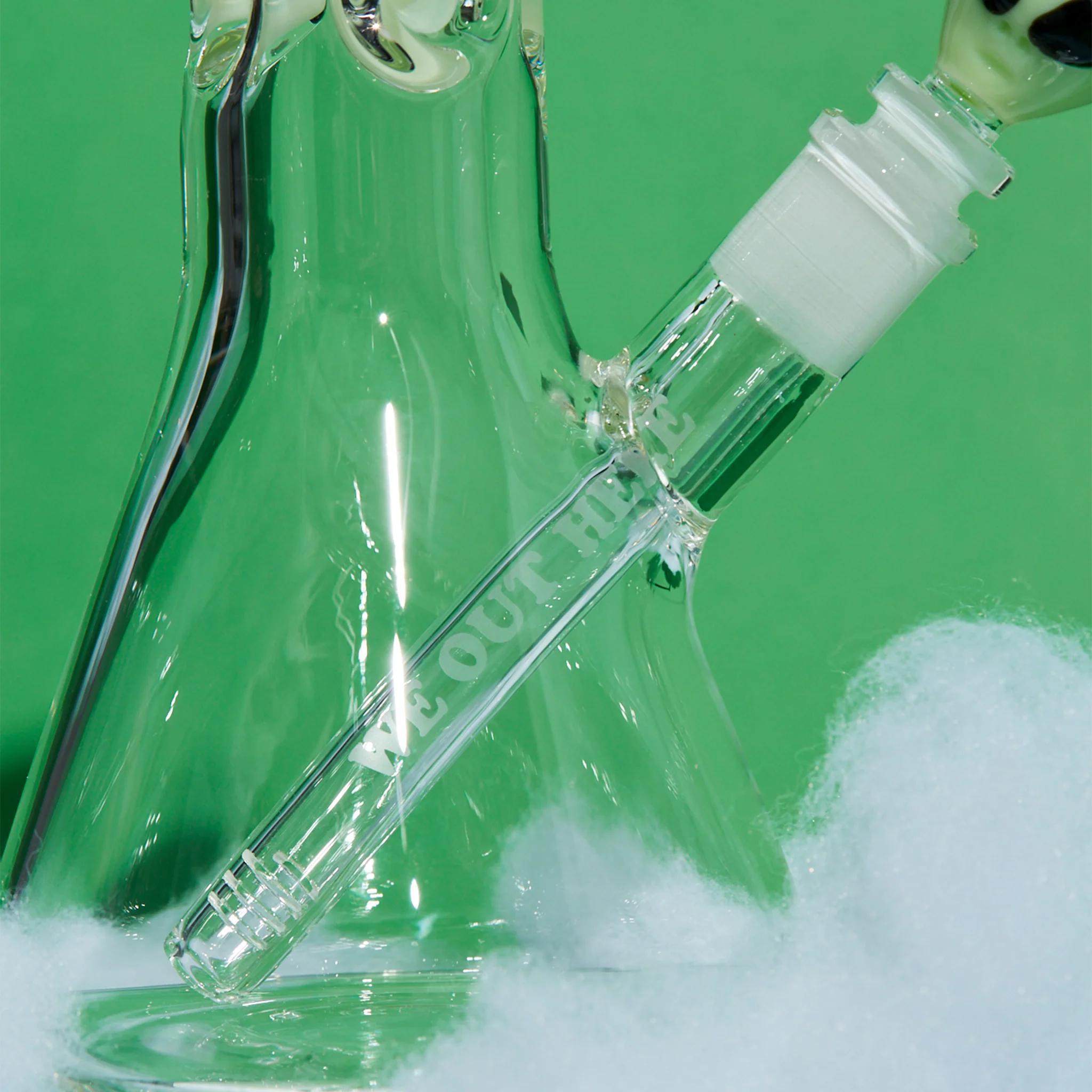 RipNDip We Out Here Beaker close-up of the glass water pipe's mouthpiece and downstem on a green background.