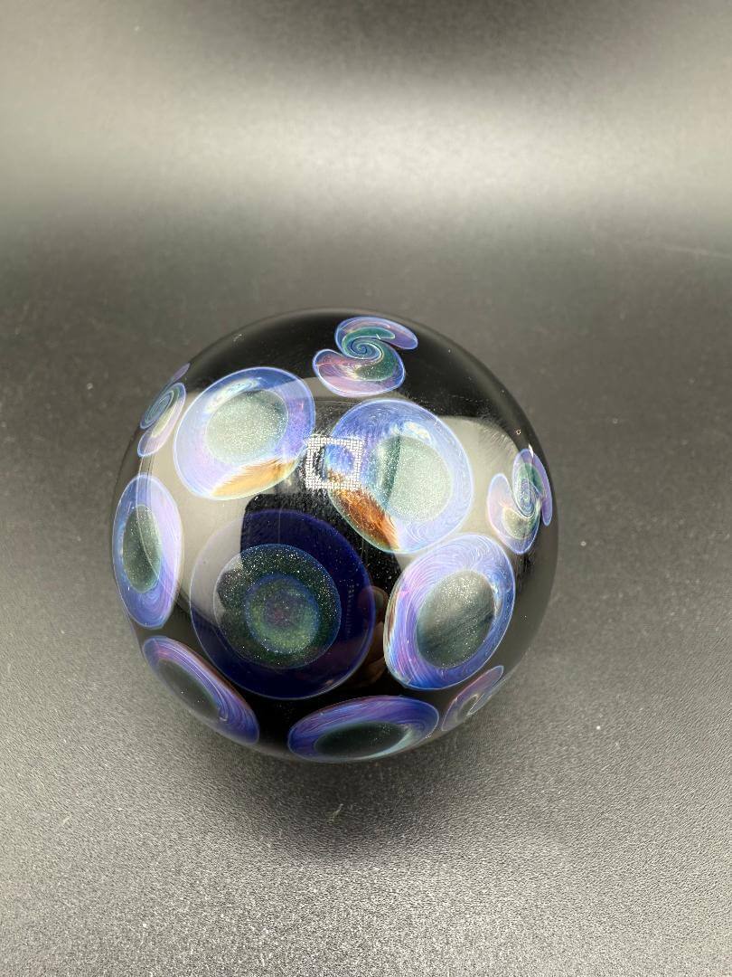 Handcrafted glass marble with colorful swirl and circle designs on a black background.