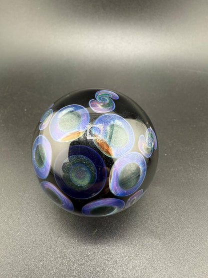 Handcrafted glass marble with colorful swirl and circle designs on a black background.