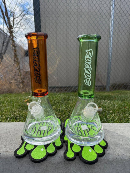Ruckus Glass 14" Thick Bottom Beaker 14mm 90° in amber and green colors displayed outdoors.