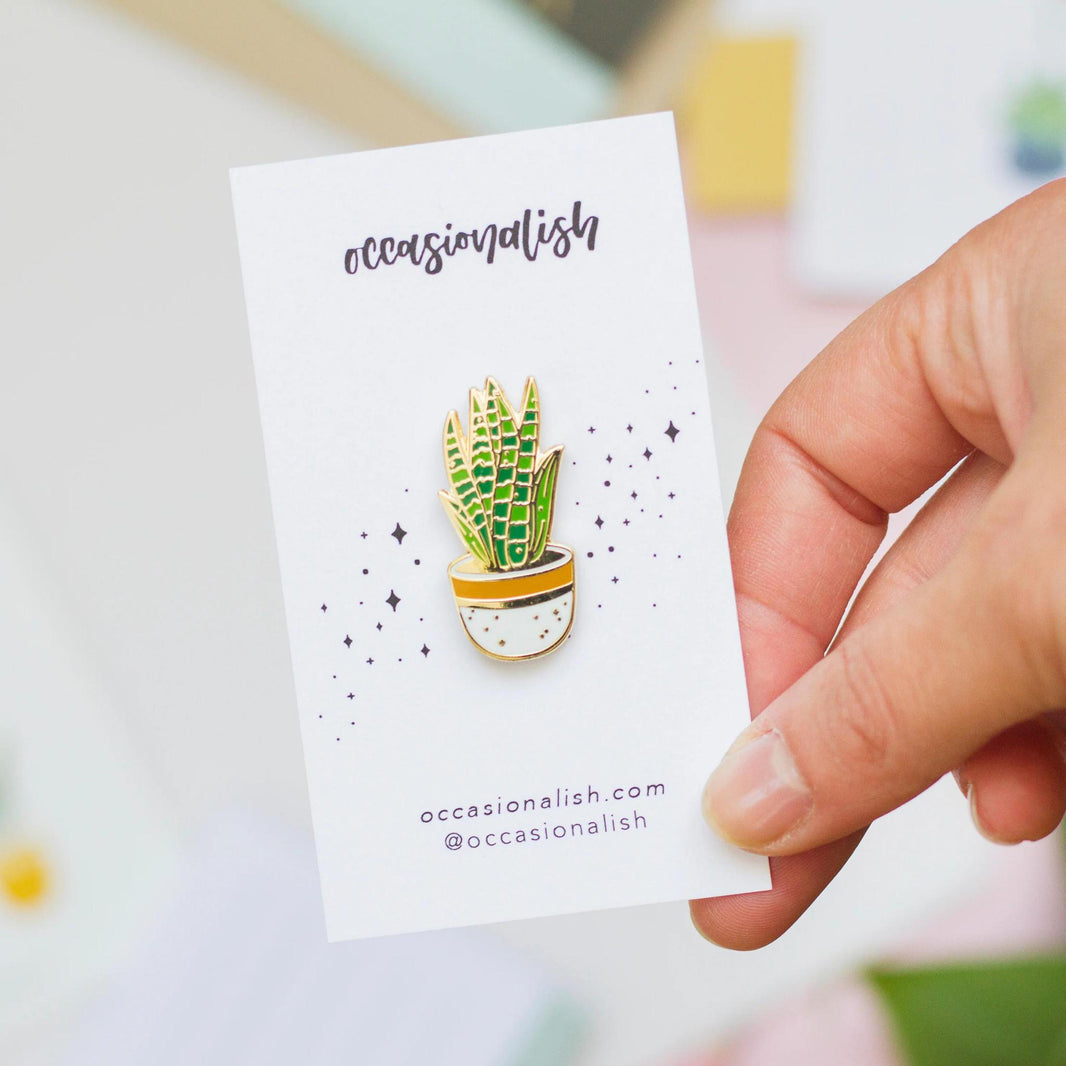 Occasionalish Enamel Pin - Snake Plant held in hand, showcasing a colorful snake plant design in a pot.