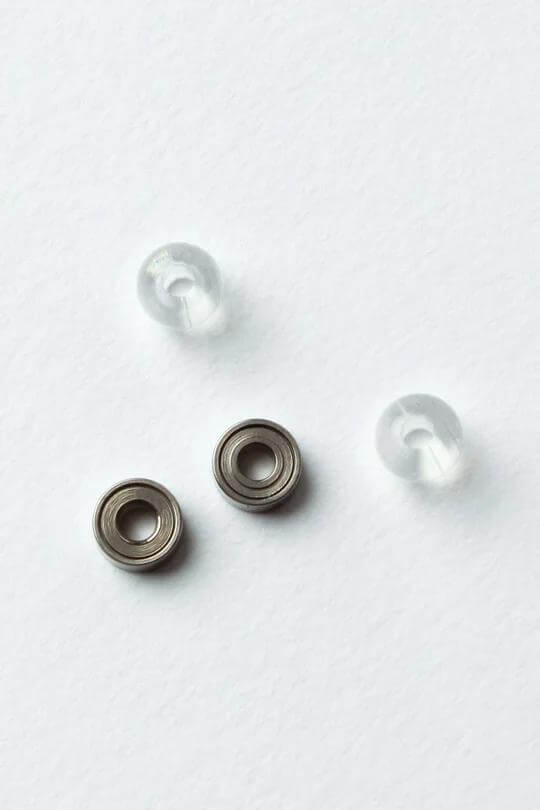 Sweets Kendama replacement parts featuring two metal bearings and two clear plastic beads on a white background.