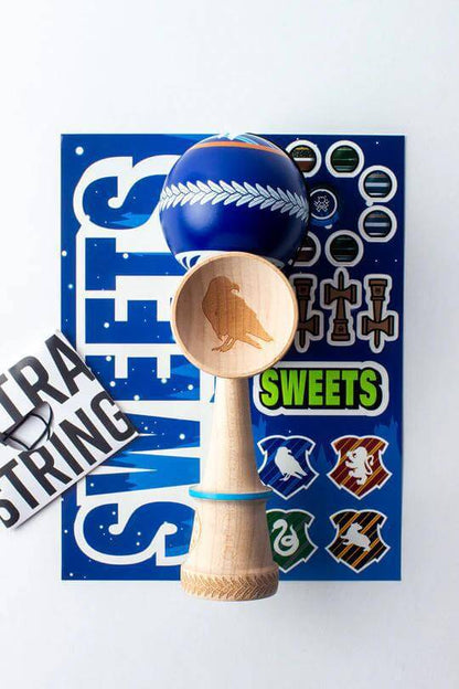 Sweets Kendama V35 Sticky Clear with engraved raven cup and colorful stickers on a vibrant blue background.