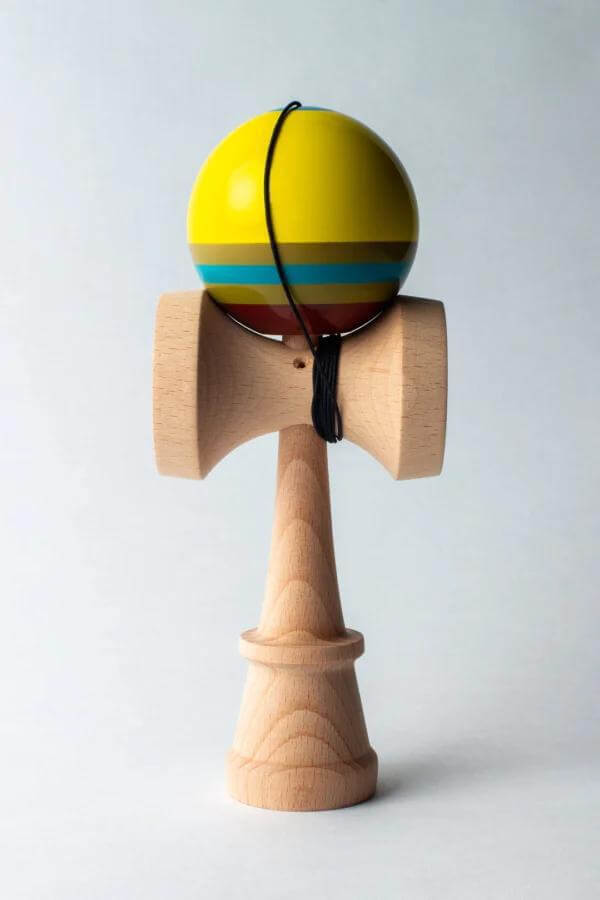 Sweets Kendama Triple Stripe with yellow tama and blue stripes on a wooden handle, showcasing modern design.