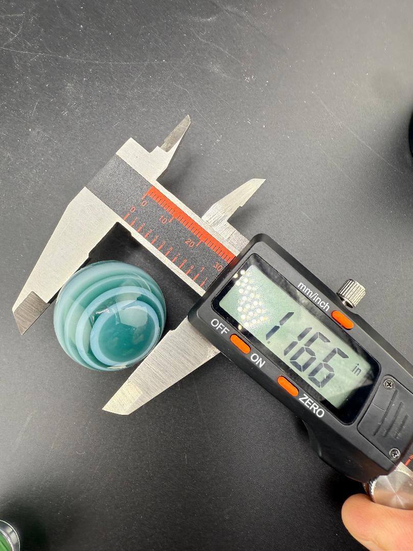 Taco Glass Marble - 2 Tone Spiral 1" measuring 1.166 inches with calipers on a black surface.