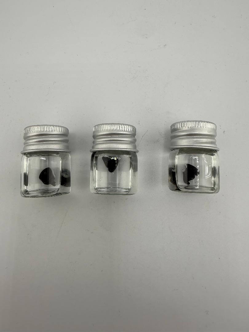 Three clear glass jars with silver lids, each containing a black heart-shaped object inside.