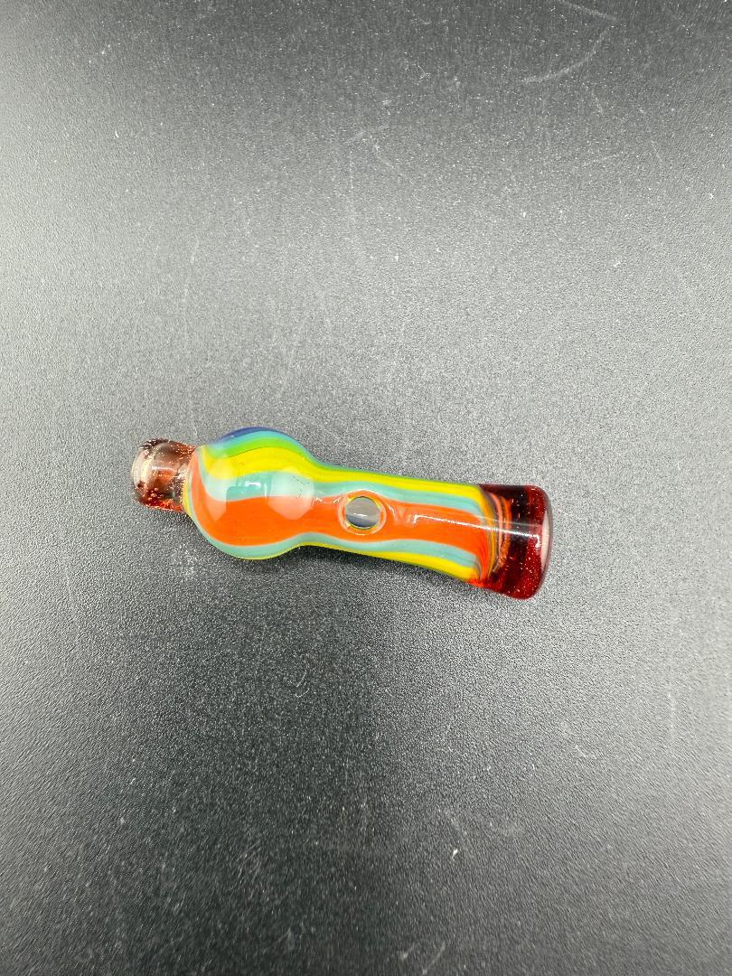 Colorful handcrafted glass piece with red, orange, green, and blue design on a black surface.