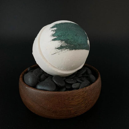 Whipped Up Wonderful - Pipe Smoke Recharge Bomb bath bomb in a wooden bowl with black pebbles.