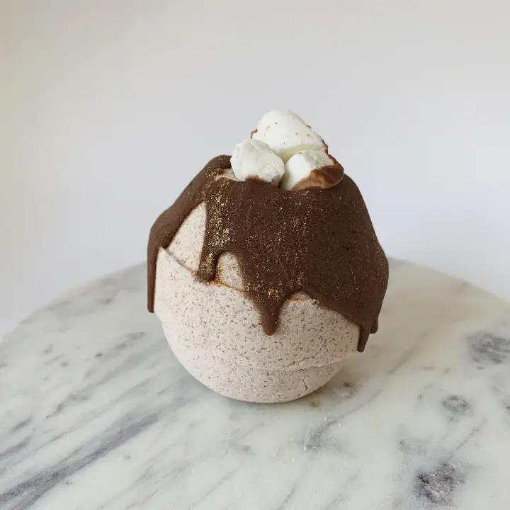 Whipped Up Wonderful White Hot Chocolate Bath Bomb topped with cocoa butter and bubble bath marshmallows on a marble surface.