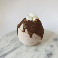 Whipped Up Wonderful White Hot Chocolate Bath Bomb topped with cocoa butter and bubble bath marshmallows on a marble surface.