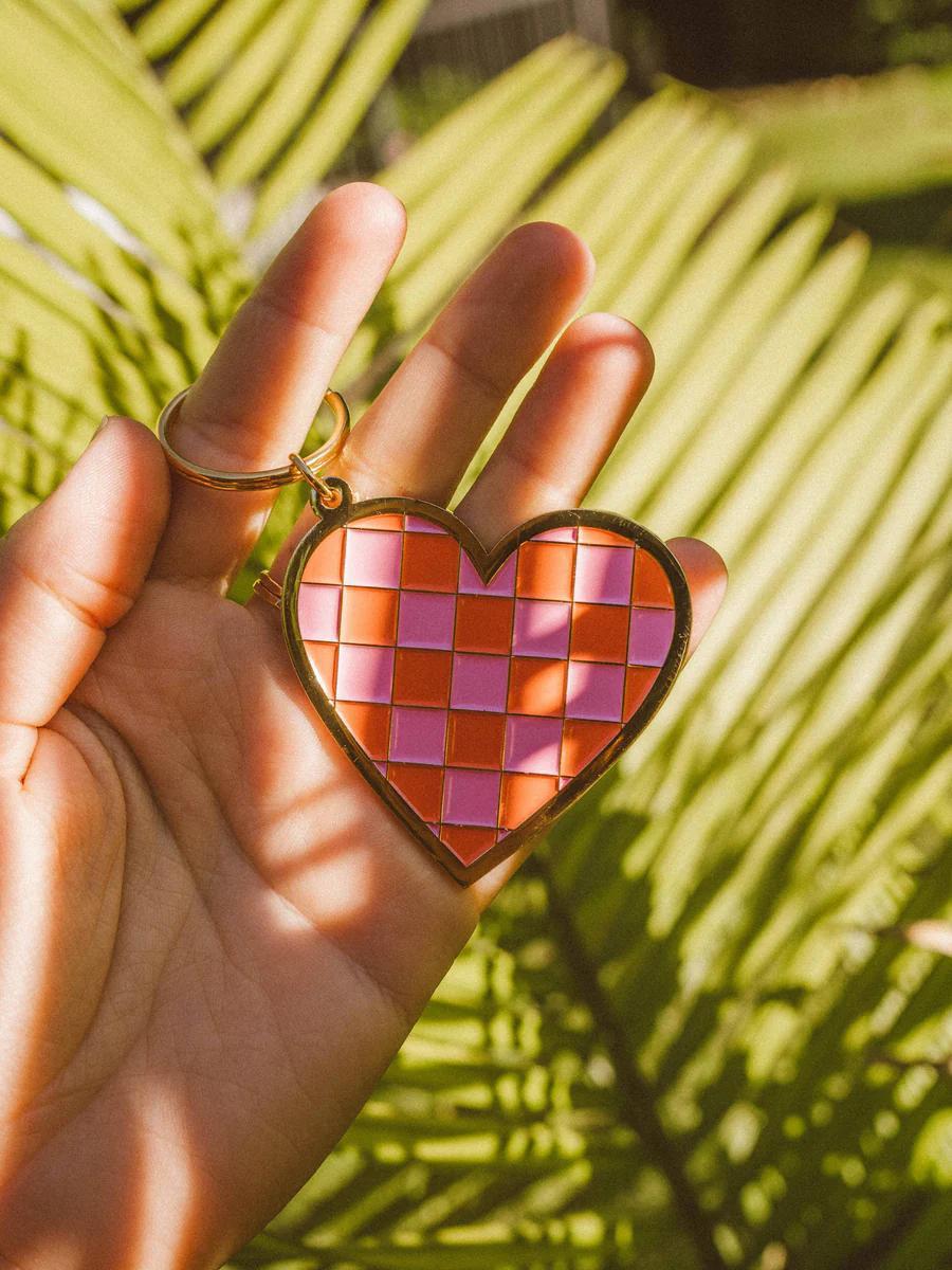 Wild Rose Keychain - Checkered Heart held in hand with palm leaves in background, showcasing vibrant design.