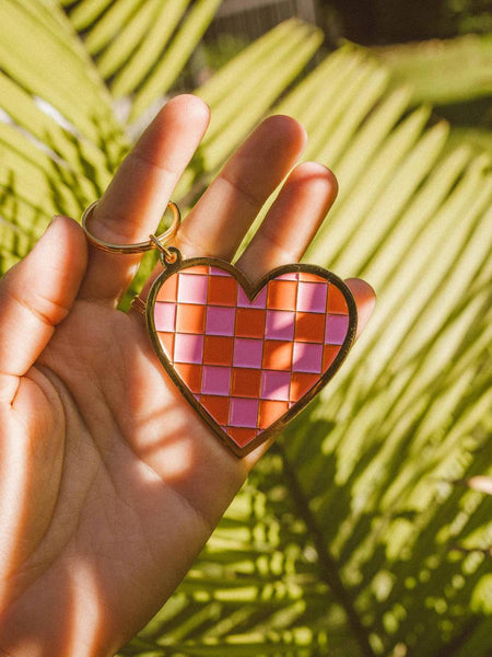 Wild Rose Keychain - Checkered Heart held in hand with palm leaves in background, showcasing vibrant design.