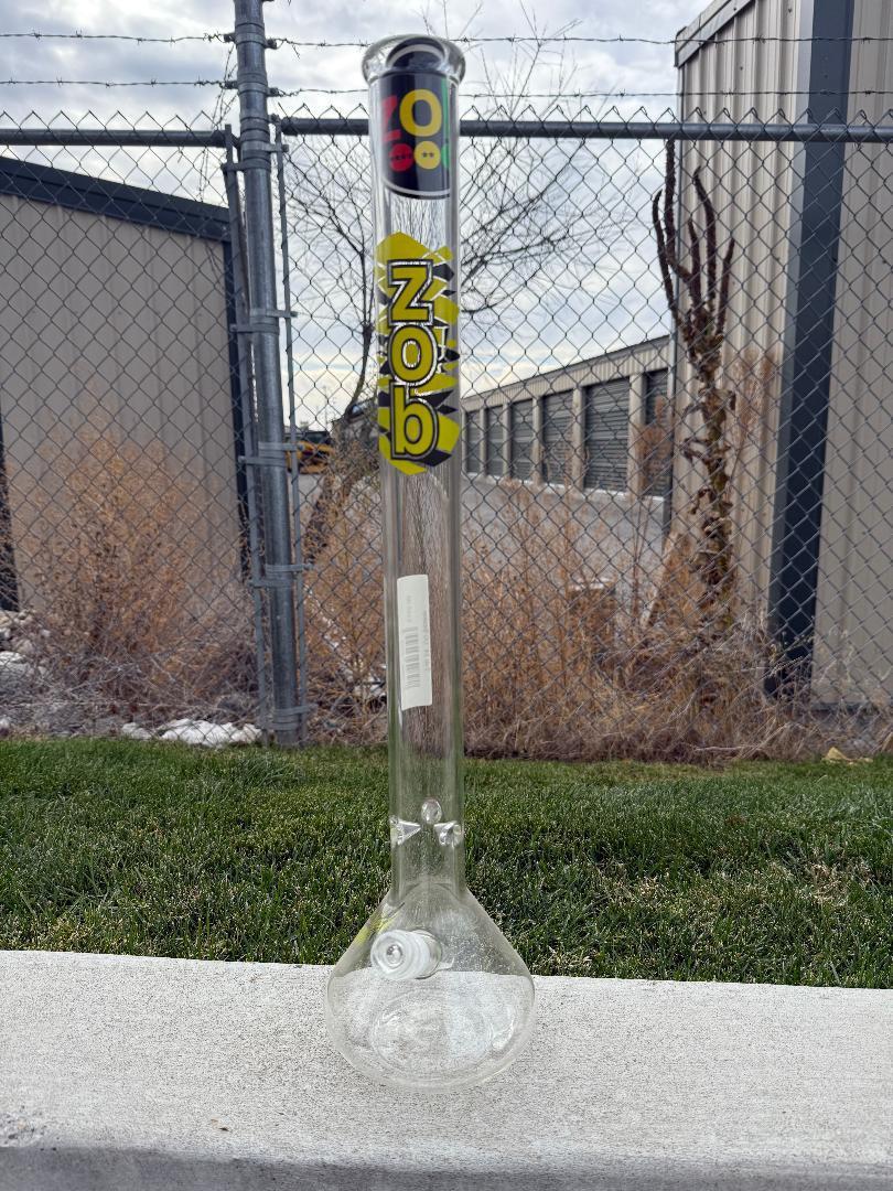 Zob Glass 24" OG Beaker Flower Piece displayed outdoors against a chain-link fence background.