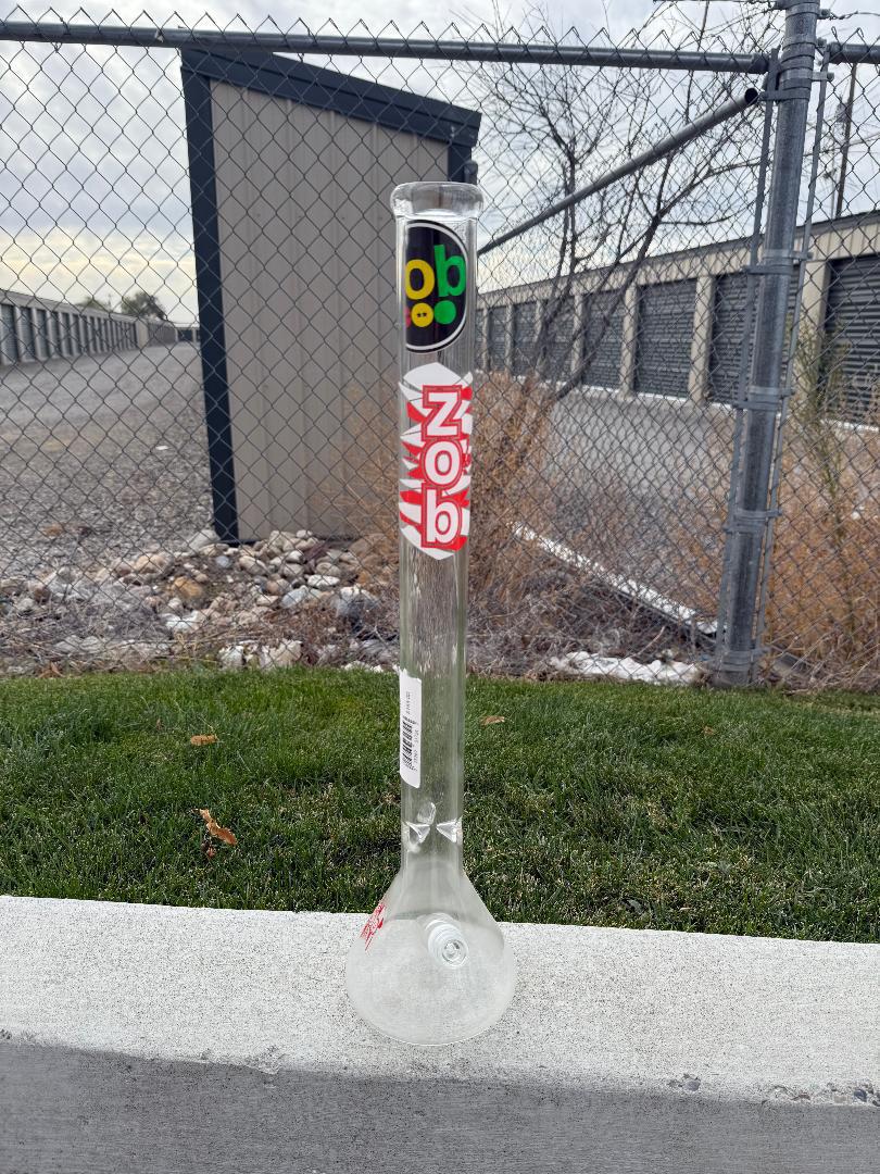 Zob Glass 24" OG Beaker Flower Piece standing on the ground against a backdrop of storage units.